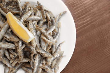 Plate with yummy fried anchovies on wooden table
