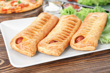 Plate with tasty sausage rolls on wooden table