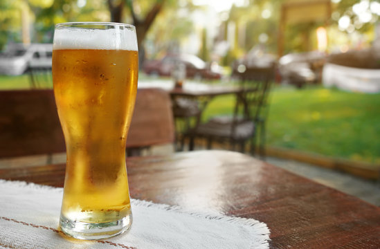 Glass of fresh beer on wooden table outdoors