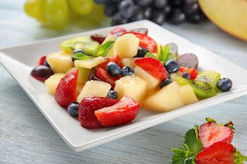 Plate with delicious fruit salad on wooden table