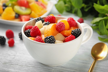 Cup with delicious fruit salad on wooden table