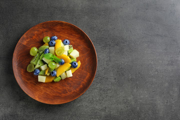 Fototapeta na wymiar Plate with delicious fruit salad on dark background