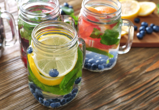 Mason jars of infused water with fruits on wooden table