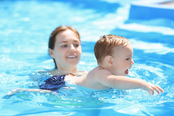 Naklejka premium Child swimming lesson. Cute little boy learning to swim with mother in pool