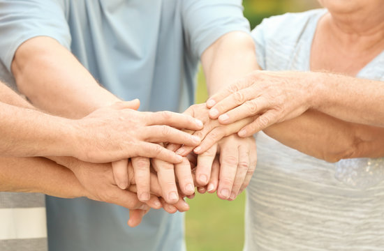 Group of elderly people in park putting hands together as symbol of unity