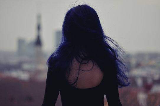 Girl with blue hair standing above city view.