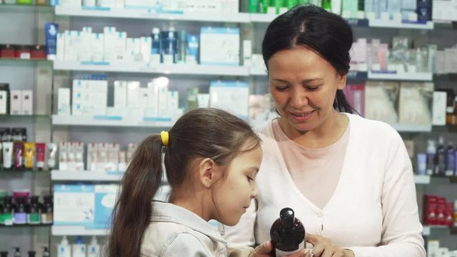 Mom and daughter are in the pharmacy. Mom reads for the daughter the name of some remedy. Daughter looks very interested. They choose something and smile