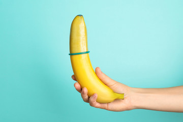Woman holding banana with condom on color background