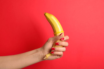 Woman holding banana with condom on red background