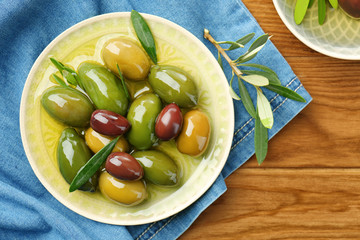 Plate with canned olives on wooden table
