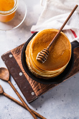 Pancakes with honey in a cast-iron frying pan on a black background, vertically