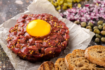 Fresh Beef Tartar is served with yolk, fried bread, pickled cucumbers and capers