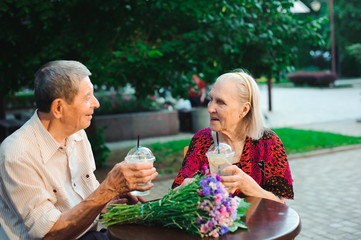 Happy elderly couple in love drinking lemonade in a cafe on the street