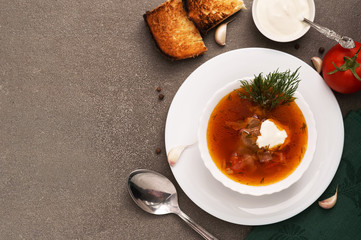 Red soup in a white plate on a gray background, top view.