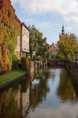 View of an idyllic canal, building full of vines in autumn colors and Love Bridge on a sunny day in Gdansk, Poland.