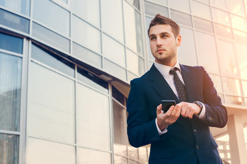 Attractive young businessman using a cell phone. Standing in front of a modern office building.