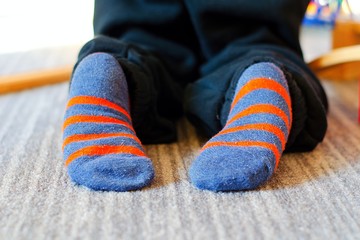 Children feet without slippers at home. Boy has only stripped socks.