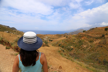 Fototapeta na wymiar Frau mit langen schwarzen Haaren und Hut schaut auf das Mittelmeer
