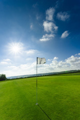 View of a green golf course, hole and flag on a bright sunny day. Sport, relax, recreation and leisure concept. Summer landscape with sunbeams - 178503396