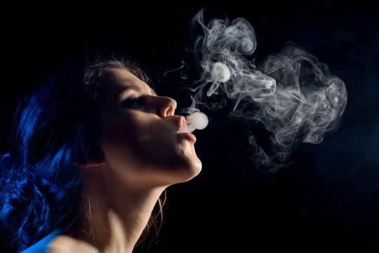young woman with clouds of smoke smoking on black background