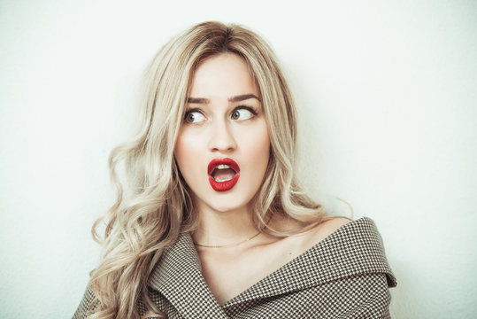 Blonde woman with long hair standing against white wall making face expressions