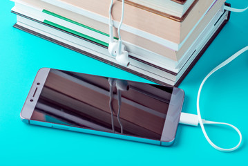 Phone with white earphones next to a stack of books on a blue background. Concept of audiobooks and modern education
