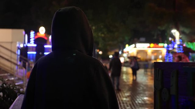 Silhouette of a man in a hood standing on a night street. 4k