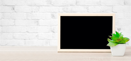 Blank chalkboard and green treepot standing on wood table and white brick wall background, space for text, mock up, product display montage