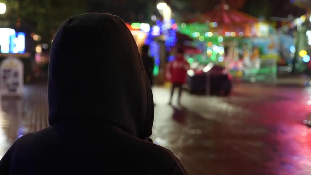 Silhouette of a man in a hood standing on a night street. 4k