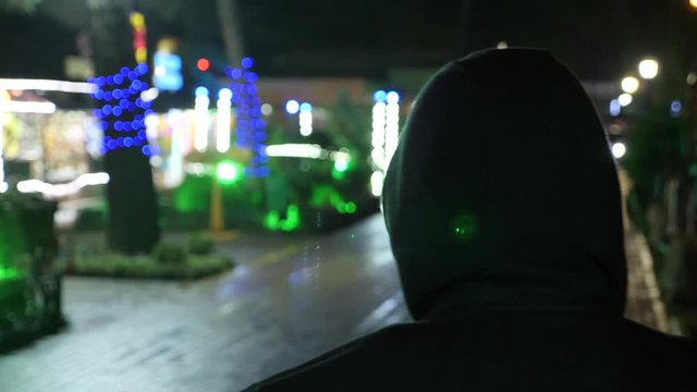 Silhouette of a man in a hood standing on a night street. 4k