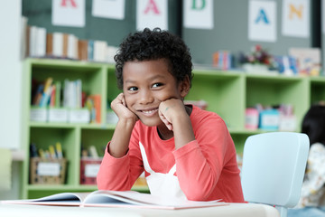 African boy sitting at his desk with smiling face in pre-elementary classroom, kindergarten, pre school education concept