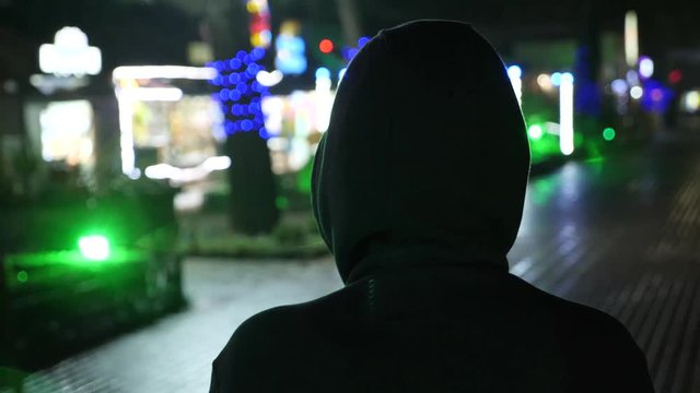 Silhouette of a man in a hood standing on a night street. 4k