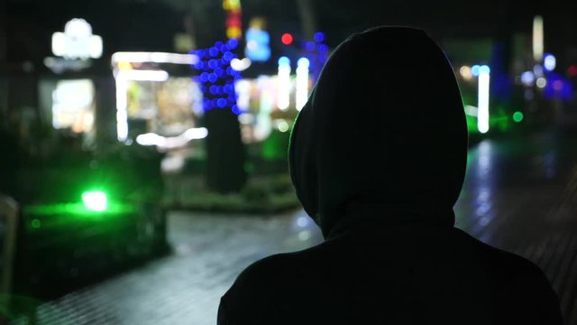 Silhouette of a man in a hood standing on a night street. 4k