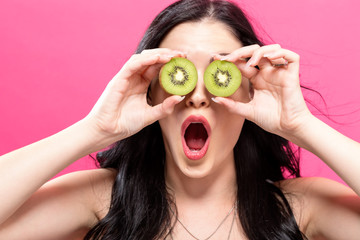  Happy young woman holding kiwis on a pink background