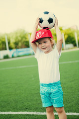 A boy in a red cap plays football at the city stadium.