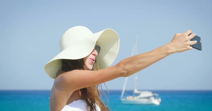 Beautiful young woman smiling, making selfie in the phone, a white bikini, sunglasses, wearing a hat, background of sea blue water and yacht. Concept: sea rest, sun, travel, vacation, freedom. enjoy.