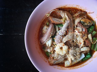 Noodles seefood Tom yum with squid and mantis shrimp, squid, prawn in a bowl on wooden table, still life and Thai style food.