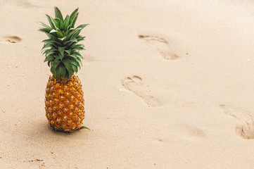 ripe pineapple on the sand and footprints