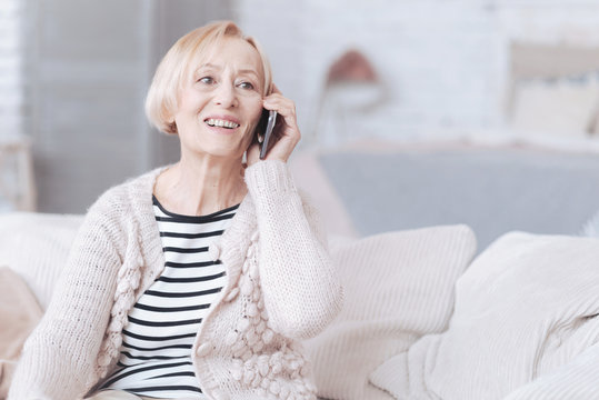 Radiant senior lady talking on phone at home
