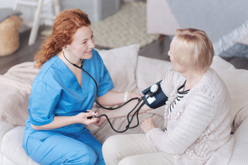 Top view of cheerful caregiver checking pressure of senior woman
