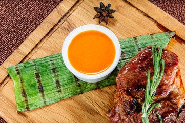 Grilled pork meat steak with yellow sauce on wooden cutting plate over wooden table