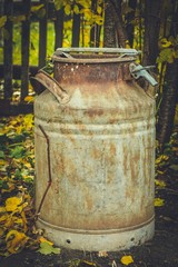 A rusty barrel stands next to a fence