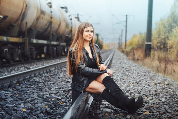 Fototapeta na wymiar Nice girl sits on a railway road in an autumn