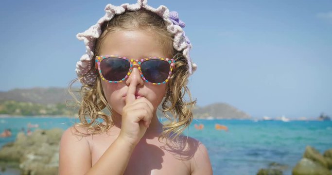 Portrait of a beautiful little girl having fun on the sea, cute smiling in sunglasses, in a panama, background of sea blue water and rocks. Concept: children, childhood, summer, freedom, kids, baby.