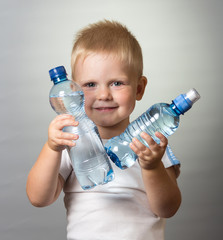 A smiling boy holds in his hands two bottles of water, on gray