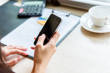 Businesswomen holding hand use smart phone with calculator and graphic document on the wooden table.