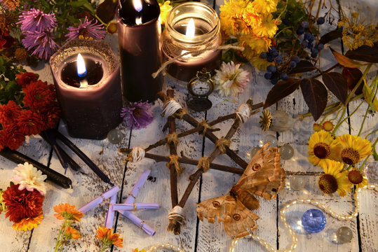 Wooden pentagram with moth, black candles and flowers on planks