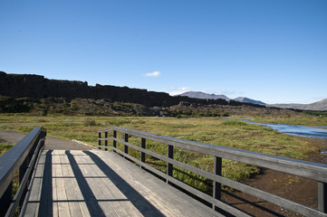 Fototapeta na wymiar National Park Thingvellir - Almannagjà canyon, Bridge in a typical Icelandic landscape, a wild nature of rocks and shrubs, rivers and lakes.