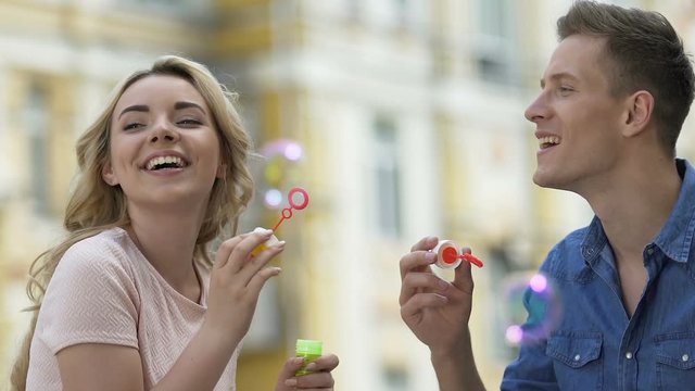 Pretty female and male blowing soap bubbles and kissing, carefree love, date