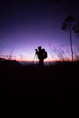 Obraz na płótnie Canvas Silhouette of photographer using tripod, taking photo of the mountain landscape with dusk sky
